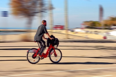 穿黑夹克的男子白天在路上骑红色摩托车